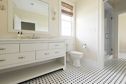 White bathroom with a vanity, toilet, shower, and black and white patterned floor.