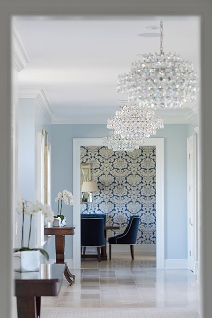 Hallway with crystal chandeliers, light blue walls, and a patterned wallpaper accent.