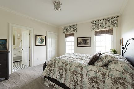 Bedroom with bed, two windows, and an attached bathroom. Neutral tones, floral patterned bedding.
