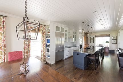 Spacious kitchen with island, built-in cabinets, and a dining table. Features hardwood floors and floral curtains.