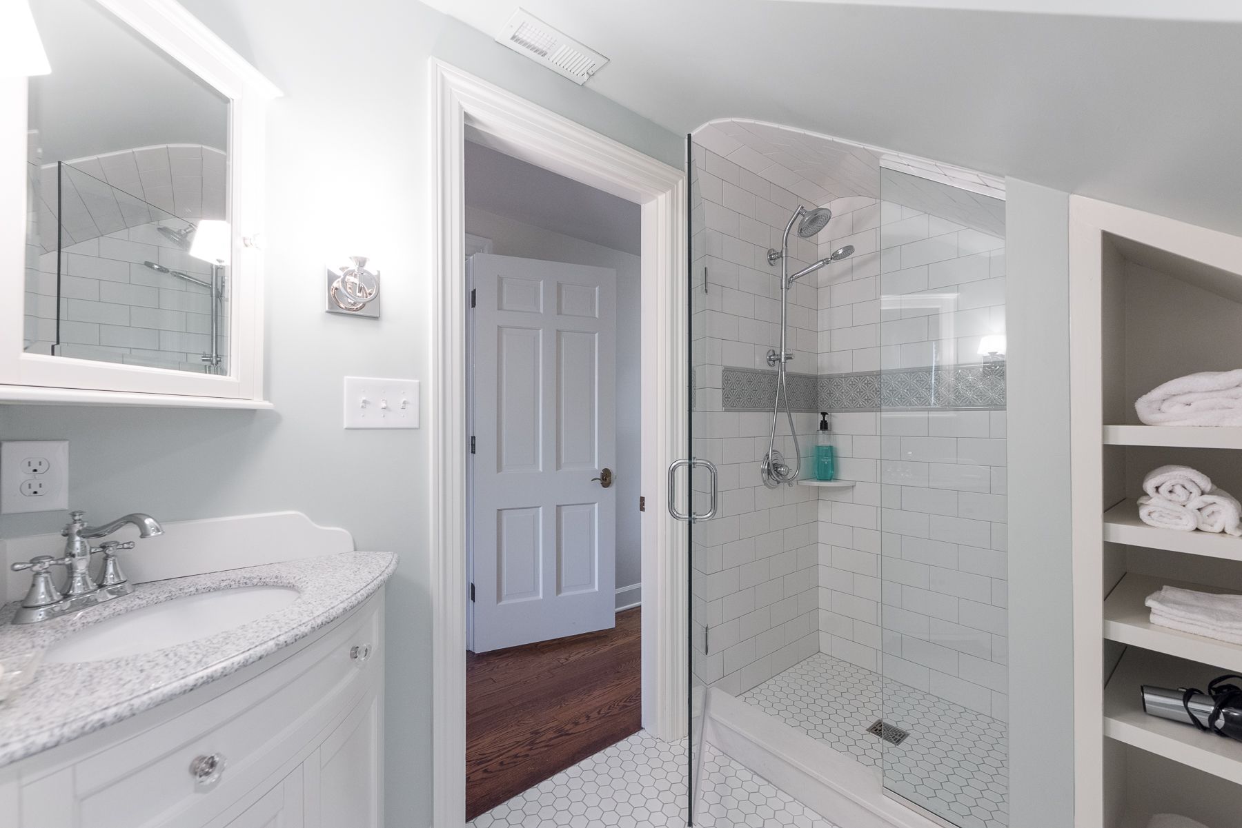 Bathroom with a glass shower, white vanity, and open door to a bedroom. Light blue walls.