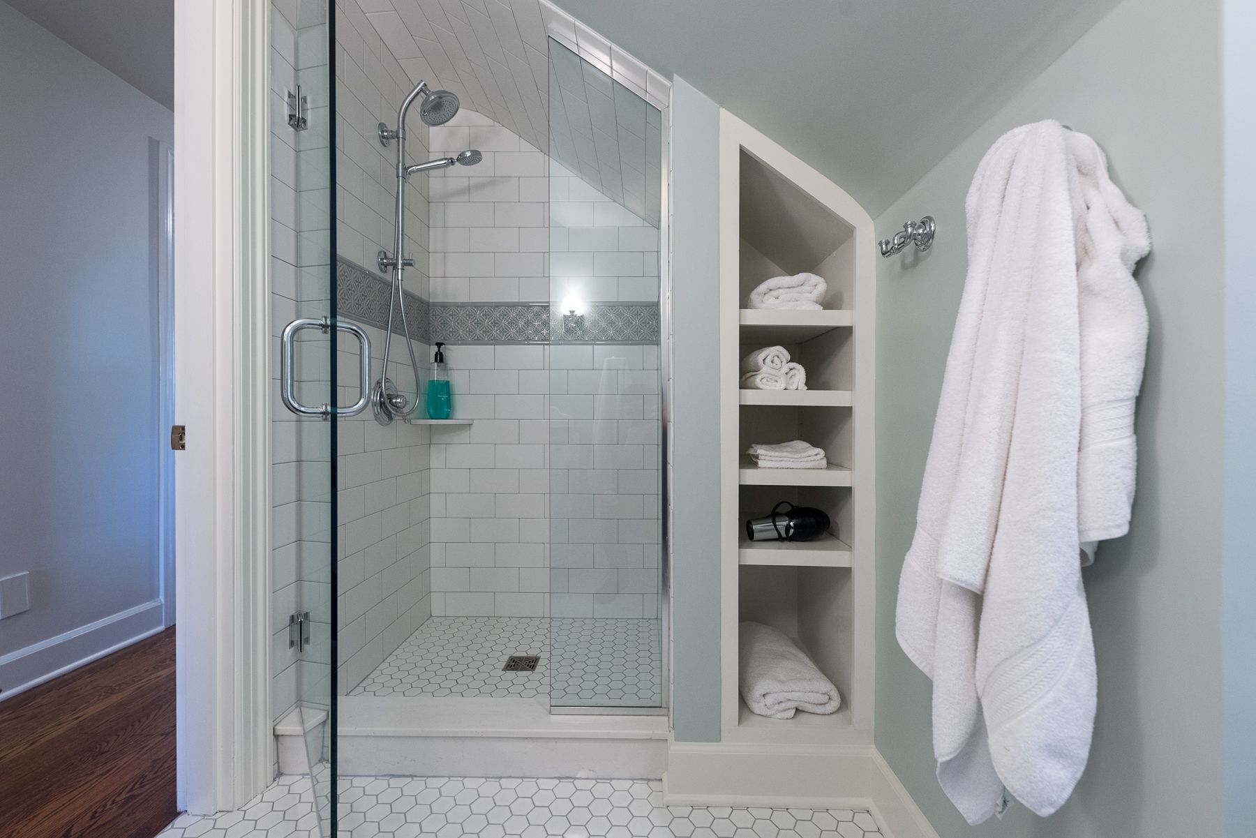 A modern bathroom with a shower, storage niche, and white towels. The walls are light blue and white.