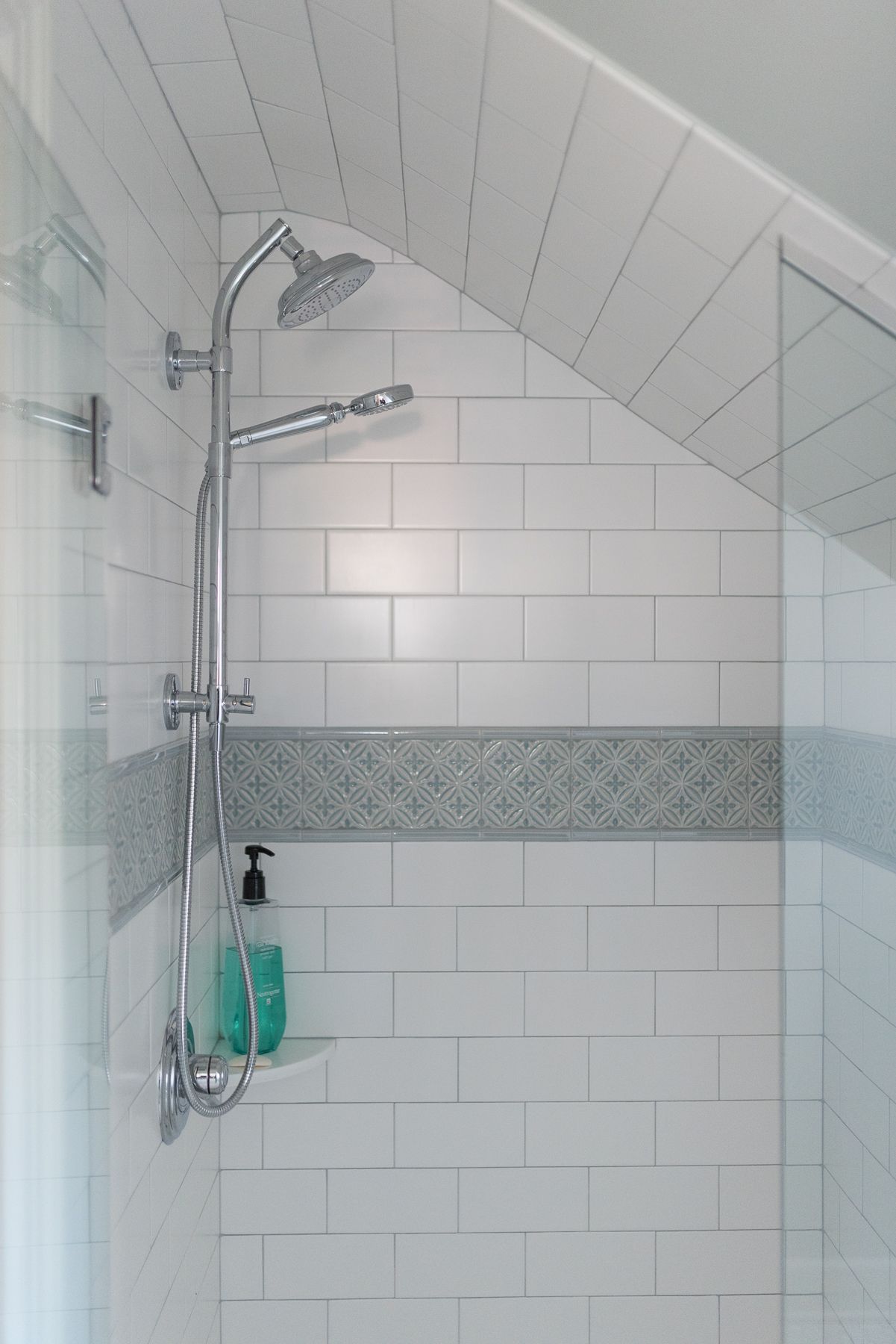 Shower with white subway tile, chrome fixtures, and a decorative tile band; angled ceiling.