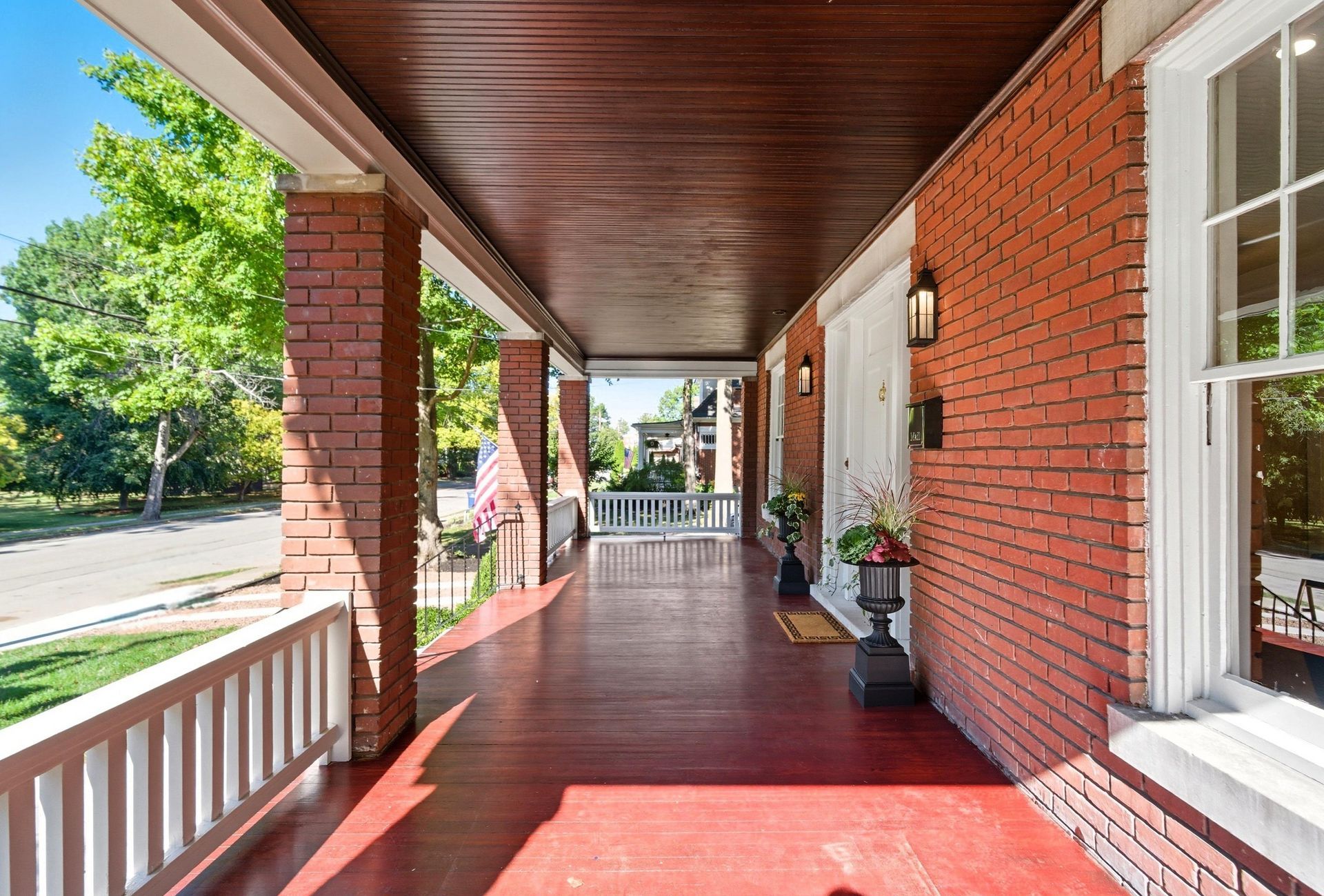 Brick porch with red floor and ceiling, white railing, and door with two black sconces.