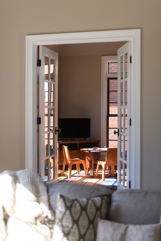 French doors open into a room with a table, chairs, and a TV, viewed from a living room sofa.