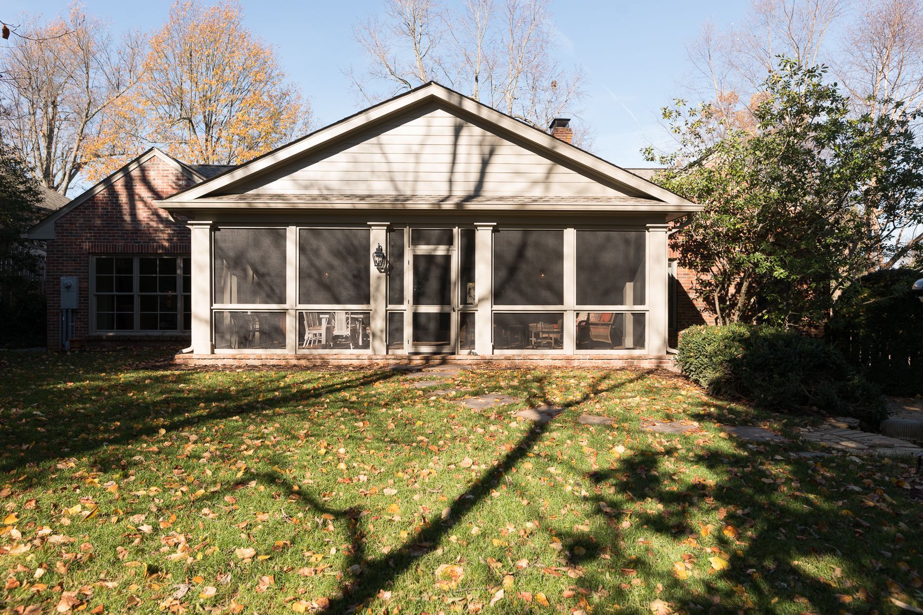 Screened porch on a brick house; sunny day with a grassy lawn and autumn leaves.