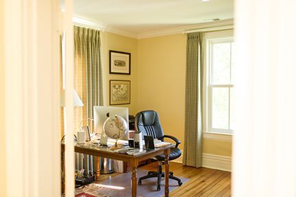 Home office with desk, computer, and chair near window, light tan walls, hardwood floor.