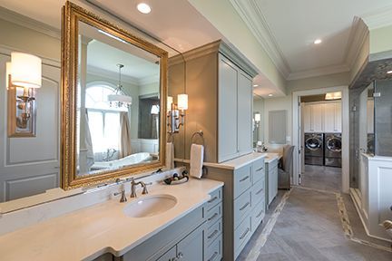 Bathroom with large gold-framed mirror, vanity with light fixtures, cabinets, and a view to laundry room.