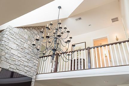 A two-story foyer with a chandelier, brick wall, and a balcony with a white railing.