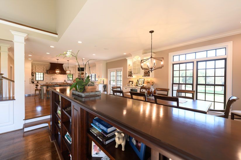 Open-concept kitchen and dining area with a long dark countertop/bookshelf, dark wood floors, and large windows.