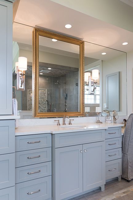 Bathroom vanity with gold-framed mirror over a countertop with light blue cabinets and sconces.
