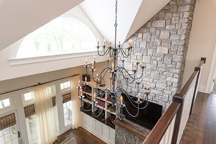 Two-story entryway with chandelier hanging above a stone wall and dark wood railing.