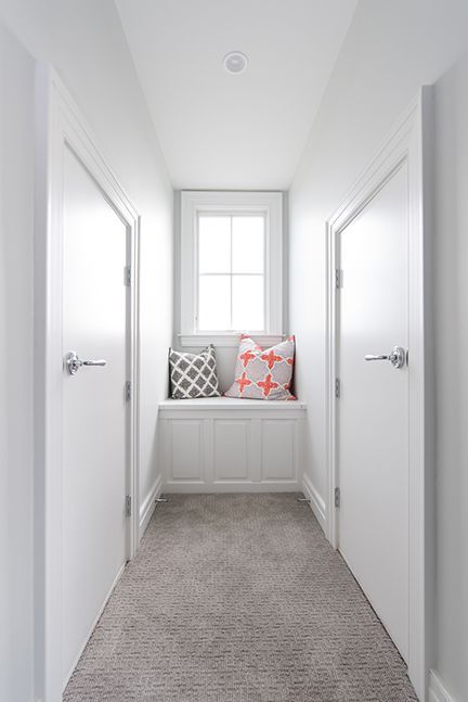Narrow hallway with white doors, built-in window seat, and gray carpet.