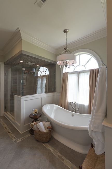 Elegant bathroom with a standalone tub, shower, arched window, and chandelier.