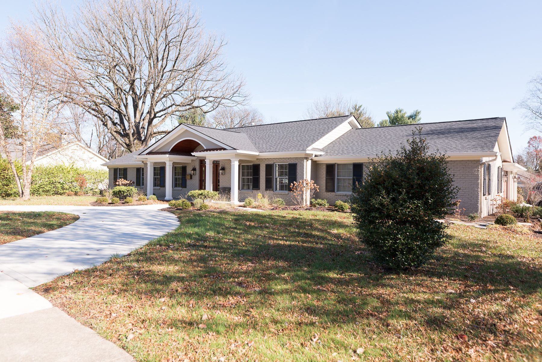 Ranch-style house with light brick, white pillars, and a curving concrete driveway. Green lawn and trees.