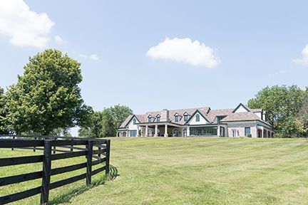 Large house on a grassy hill with a black fence in the foreground, sunny day.