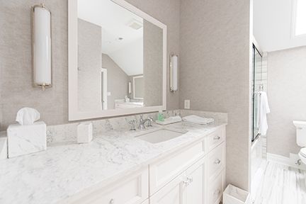 White bathroom with marble countertop, large mirror, and neutral walls.