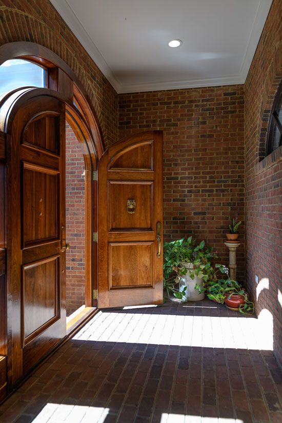 Open, arched wooden doors lead into a brick-walled entry with plants.
