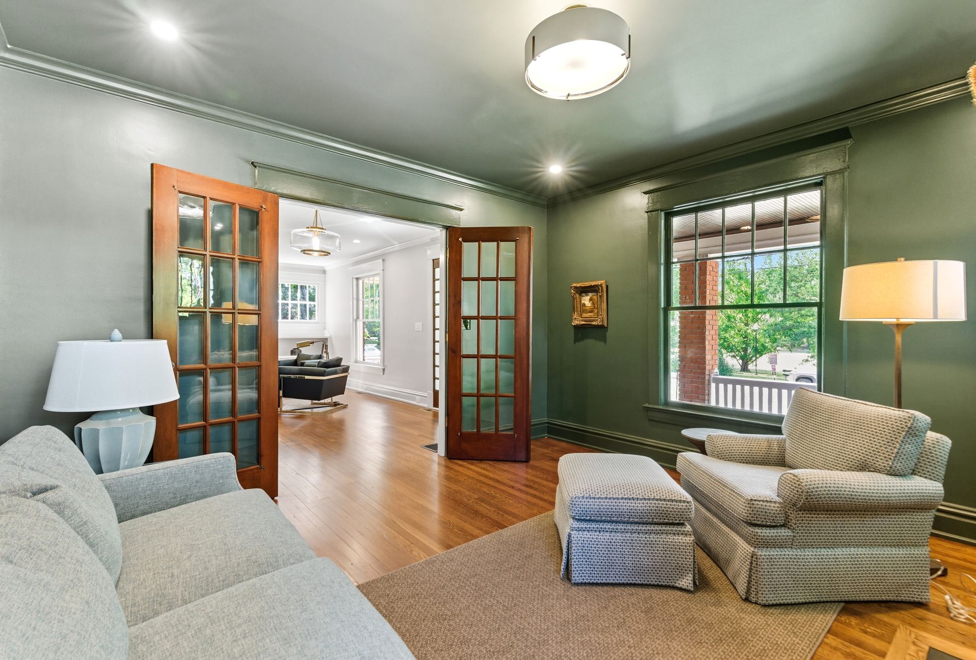 Living room with sage green walls, hardwood floors, and a seating area with a sofa, armchair, and ottoman.