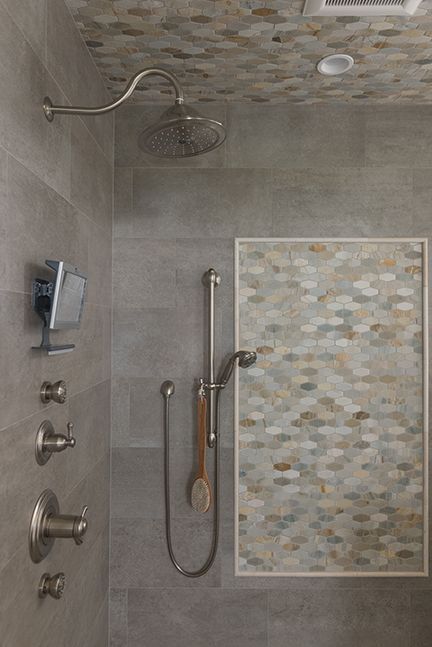 Shower with gray tiles, decorative tile inset, and various showerheads and controls.