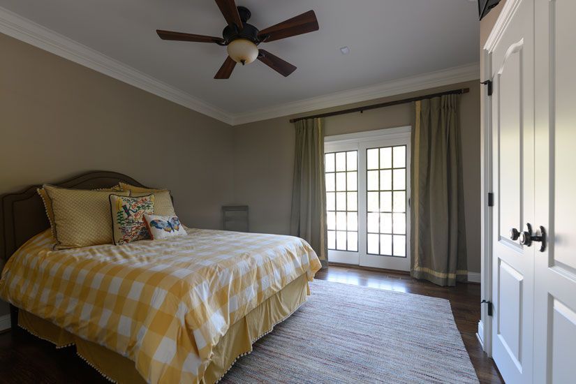 Bedroom with yellow plaid bedding, French doors, and a ceiling fan.