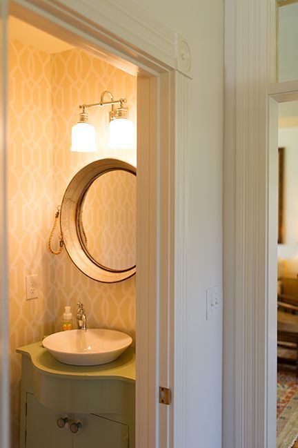 Small powder room with patterned wallpaper, a round mirror, and a light green vanity.