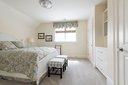Bedroom with a white bed, floral bedding, window, and built-in cabinets, soft light.