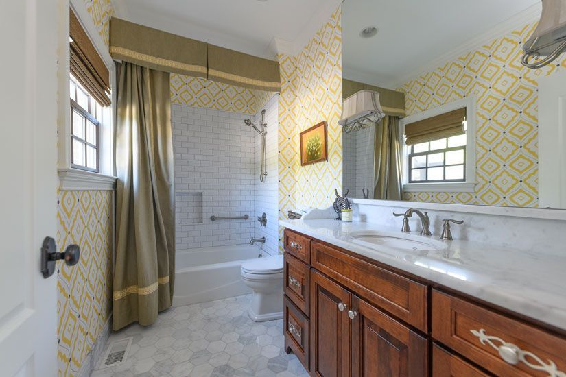 Bathroom with yellow patterned wallpaper, wood vanity, and white tiled shower.