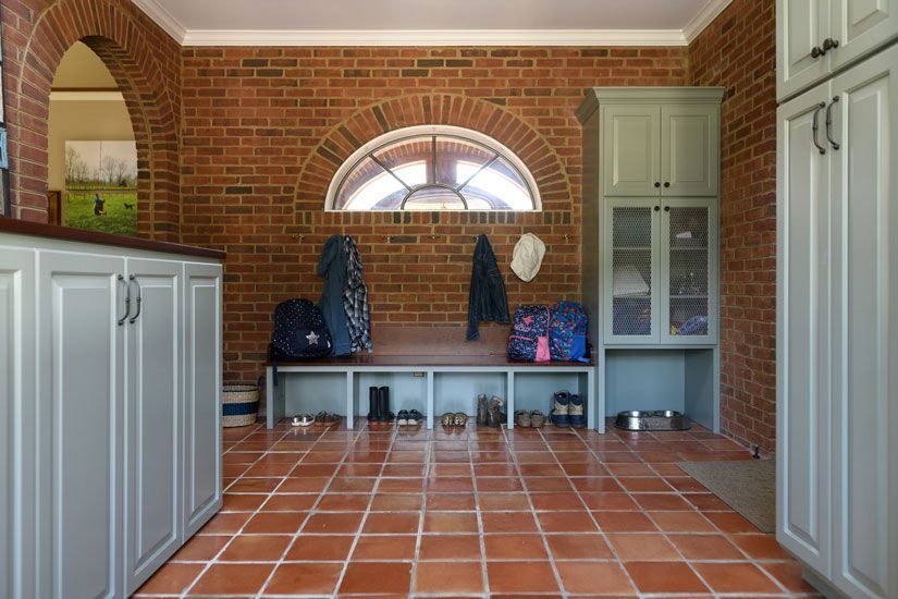 Mudroom with brick walls, terra-cotta tile floor, benches, and storage cabinets; bags, jackets, and shoes present.