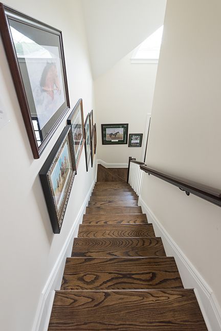 Wooden staircase with framed pictures on the wall, dark wood railing on the right.