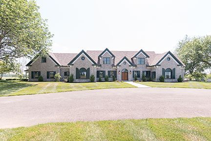 Large brick house with dark shutters, brown roof, and manicured lawn.