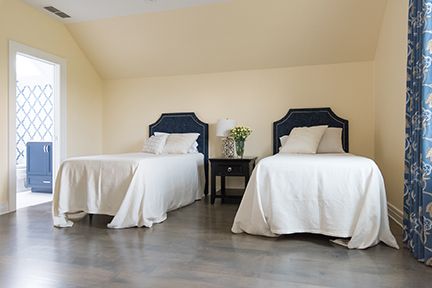 Two twin beds in a bedroom with a nightstand. Pale yellow walls and gray wood floor. Blue headboards.