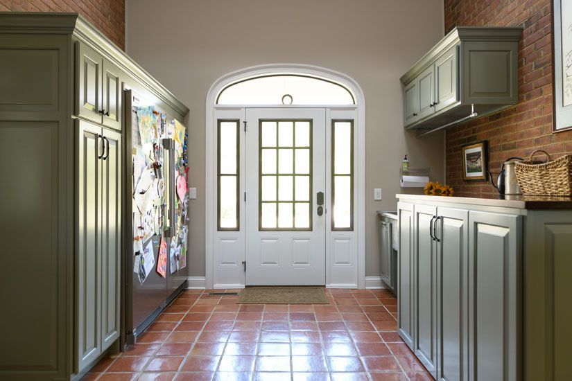 Hallway with olive cabinets, red tile floor, white arched door. Red brick wall.