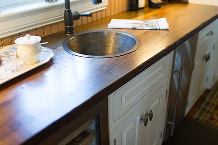 Wooden countertop with a round sink, white cabinets, and a window in a kitchen.