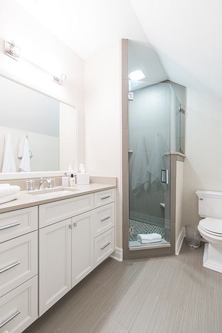 Bathroom with a white vanity, gray flooring, and a glass shower under a sloped ceiling.