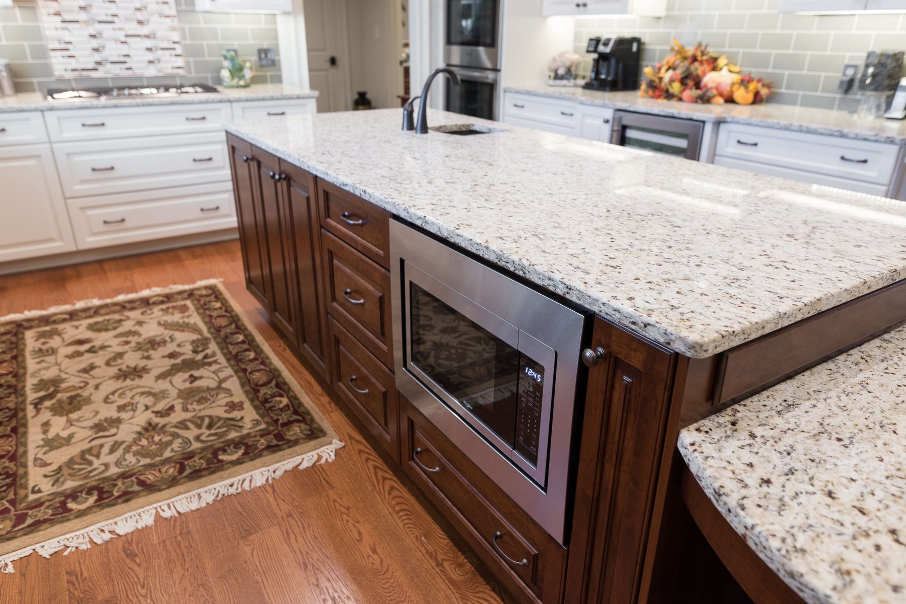 Kitchen island with microwave, granite countertop, and wood cabinets, in a well-lit kitchen.