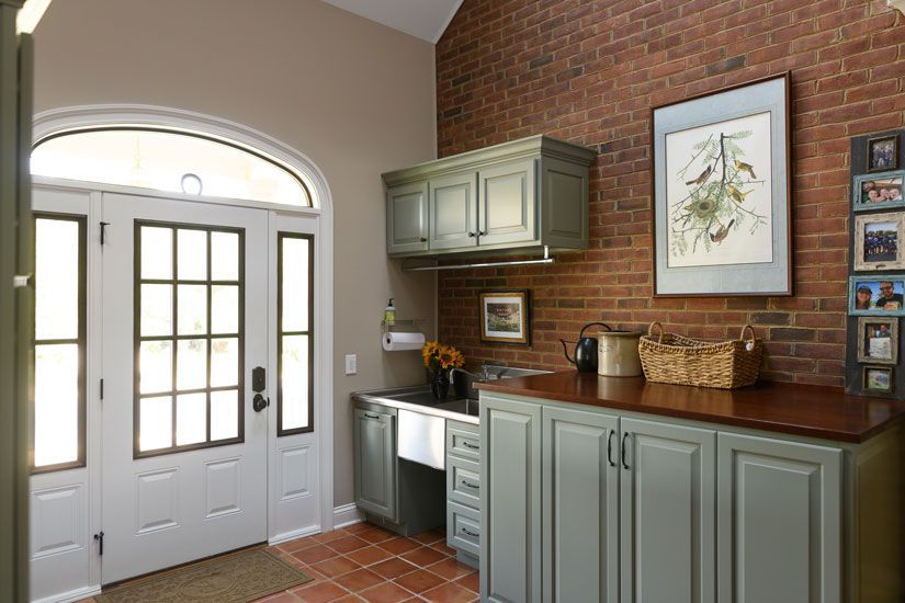 A laundry room with a brick wall, sage green cabinets, a stainless steel sink, and a double door.