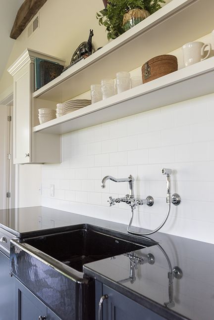 Kitchen sink with black countertop, white subway tile backsplash, and open shelving.