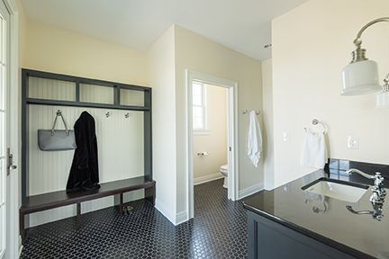 Mudroom with coat rack, bench, and powder room. Black tile floor, black countertop, and light walls.