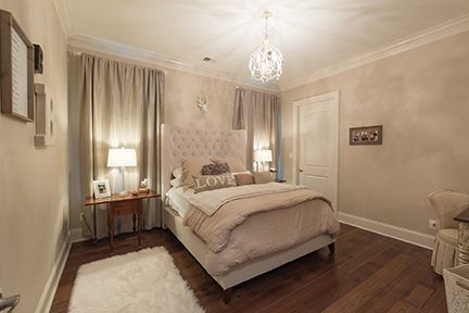 Bedroom with a tufted headboard, soft colors, wood floors, and a decorative chandelier.