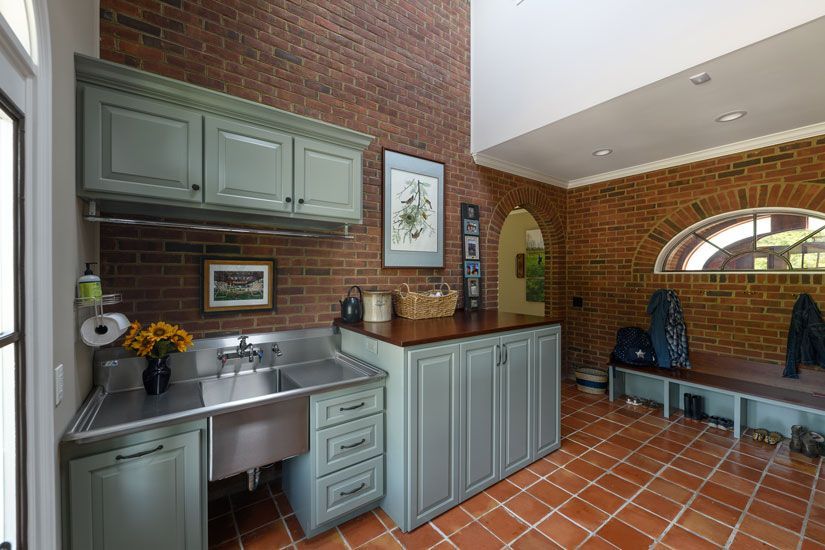 Laundry room with brick walls, stainless steel sink, green cabinets, and red tile floor.