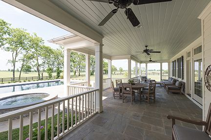 Covered patio with pool, dining, seating. Light blue ceiling, stone floor, white pillars, rural setting.