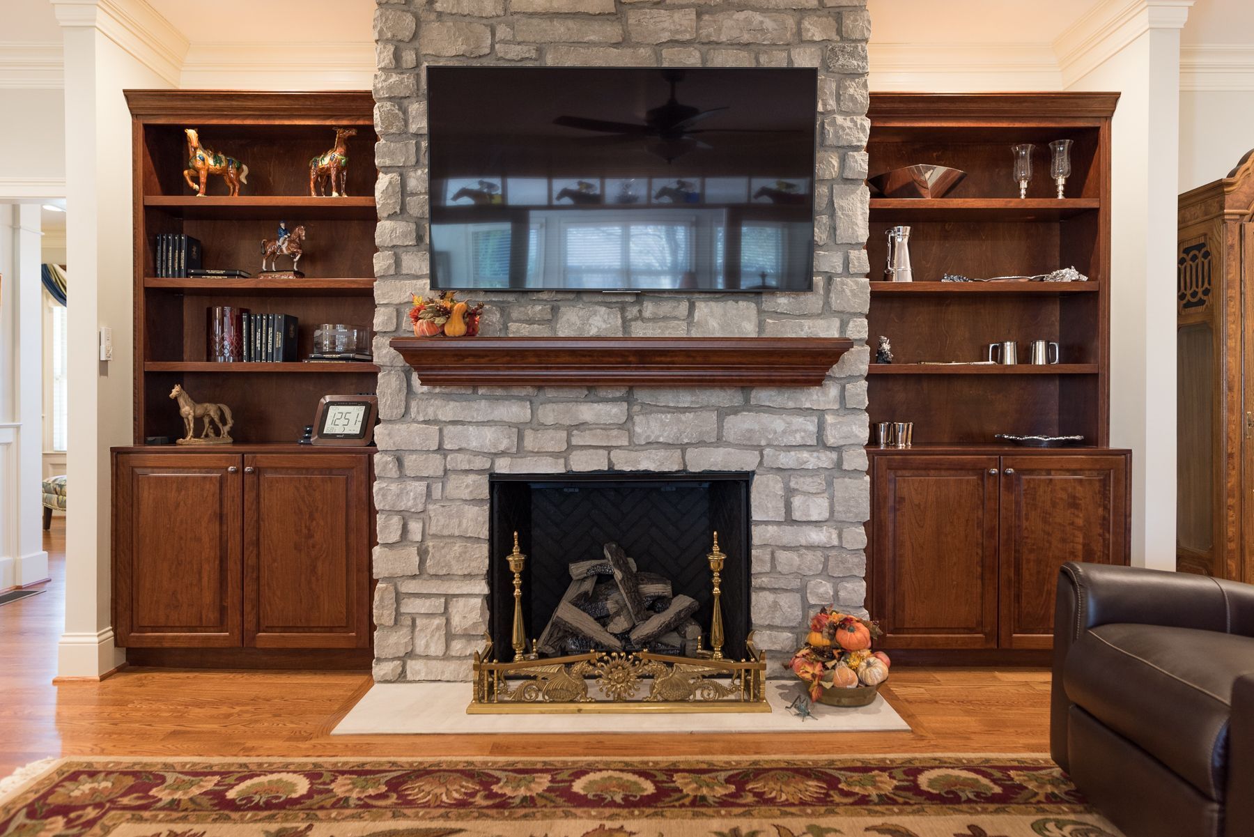 Fireplace with built-in bookshelves, TV mounted above, stone surround, wooden mantel, hardwood floor, and a sofa.