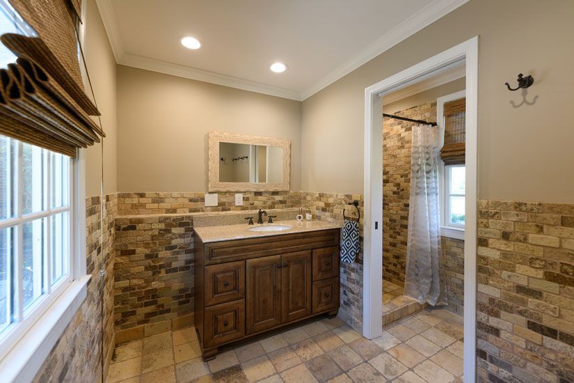 Bathroom with stone tile walls, a wooden vanity, and a shower.