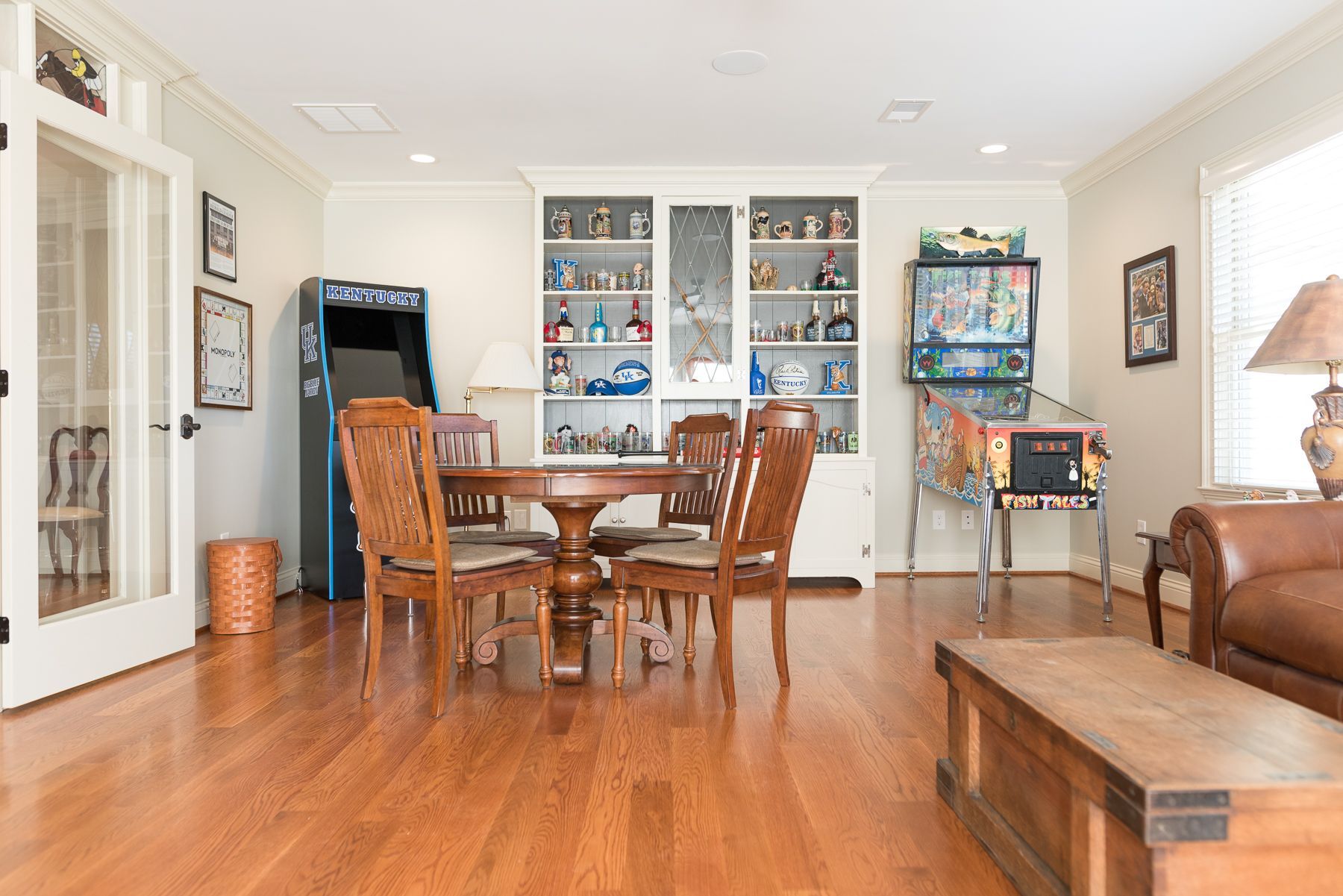 Living room with arcade game, pinball machine, table, chairs, and display shelves.