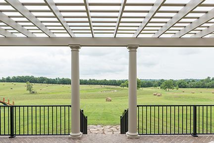 View from a porch with columns and a lattice roof overlooking a green field with hay bales.