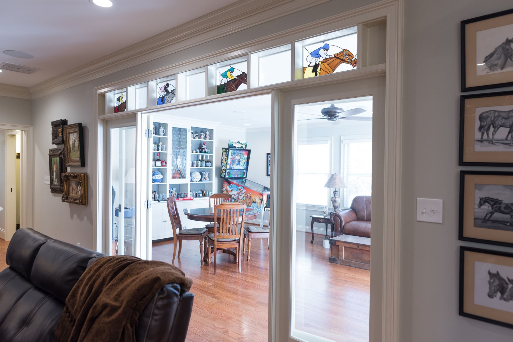 Open doorway into dining room with stained glass, wooden floors. Living room with leather couch and framed art.