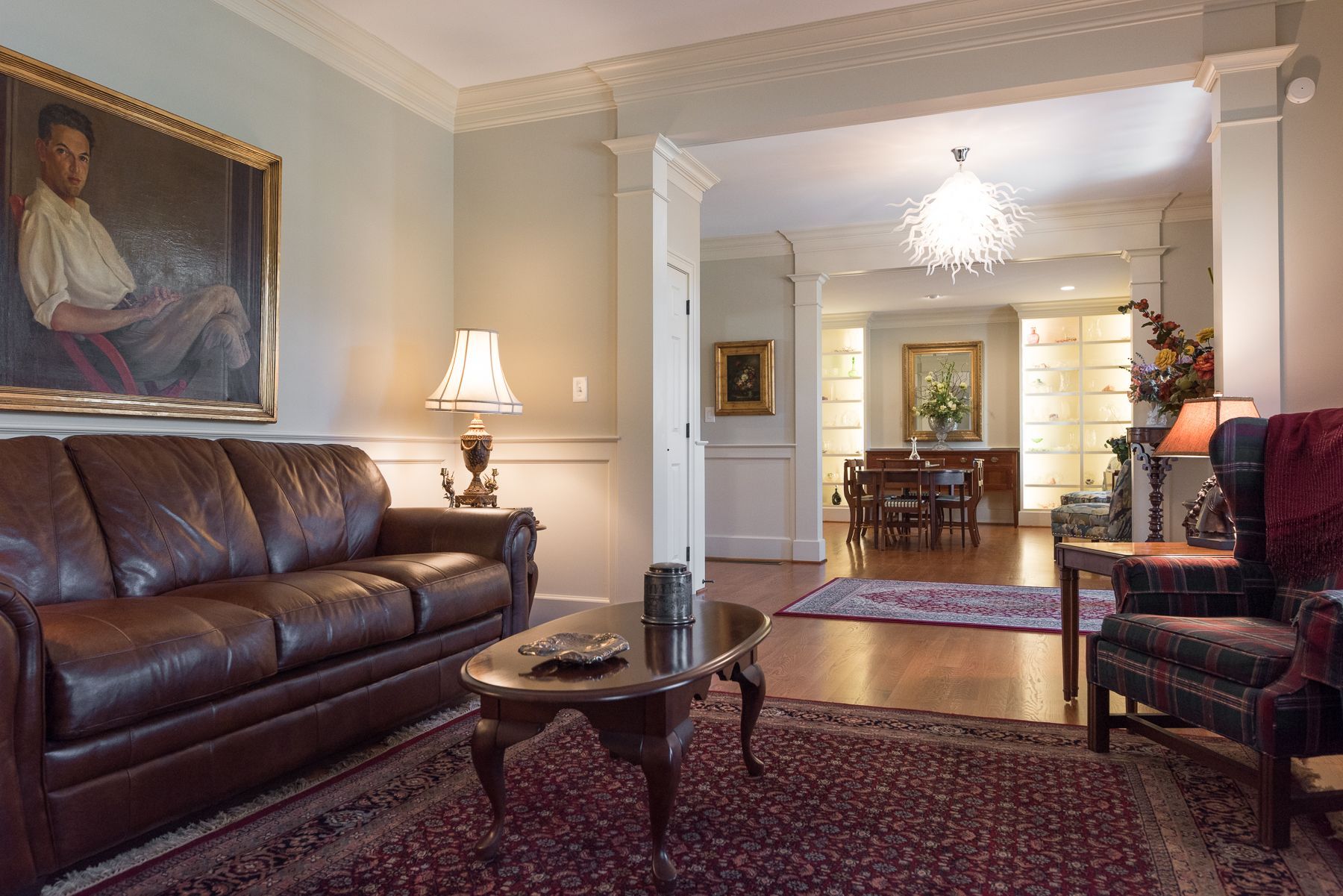 Living room with brown leather sofa, area rug, and artwork, opening to dining area.