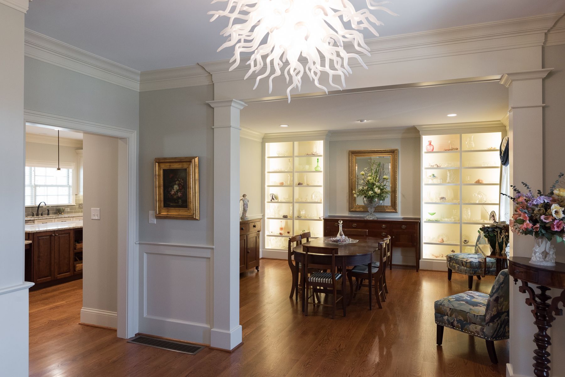 Elegant dining room with wood floors, built-in shelves, and a decorative chandelier.