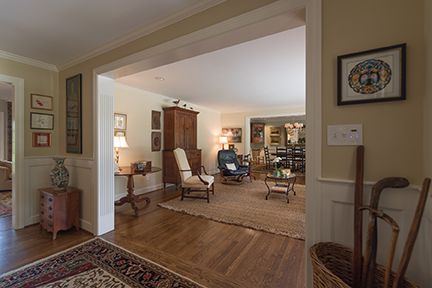 Entryway with hardwood floors, leading to a living room with a rug, chairs, and dining room in the background.